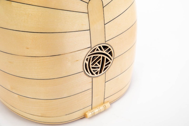 May include: A close-up of the back of a light wood musical instrument with a decorative sound hole. The sound hole is a circle with a geometric design.