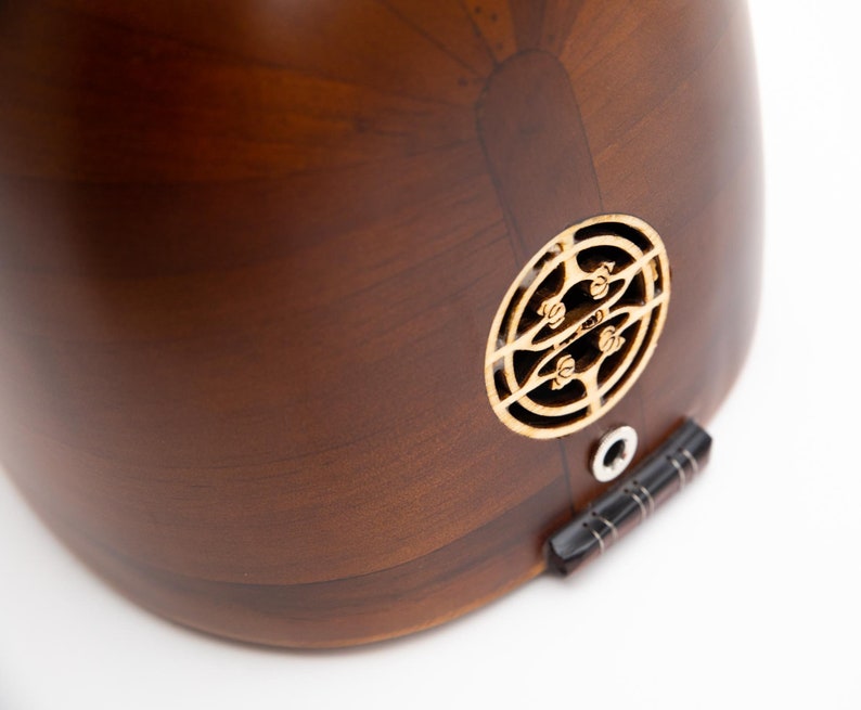 May include: Close-up of a wooden stringed instrument, likely a lute or oud, with a dark brown finish. The instrument features a decorative sound hole and a black bridge. The wood grain is visible, and the instrument appears to be well-crafted.