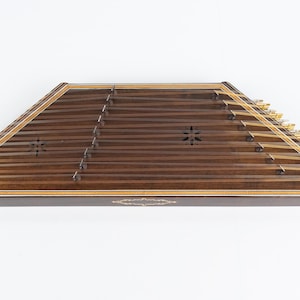 May include: A wooden santur, a hammered dulcimer, with a dark brown finish and gold tuning pegs. The instrument has a decorative inlay around the edge.
