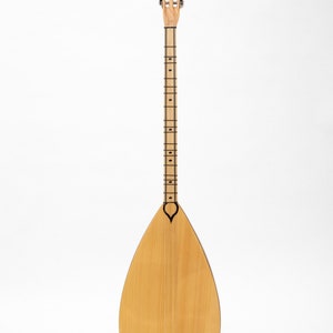 May include: A wooden saz, a traditional Turkish stringed instrument, with a pear-shaped body and a long neck with tuning pegs. The saz is on a black stand against a white background.