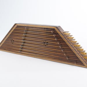 May include: A wooden santur, a trapezoidal hammered dulcimer with a dark brown wood finish and intricate inlaid designs. The instrument has 10 strings and a set of metal tines on the right side.