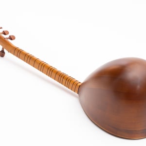 May include: A wooden stringed instrument with a long neck and a rounded body. The instrument is a warm brown color, with a lighter-colored neck and tuning pegs. The body features a decorative gold-colored sound hole.