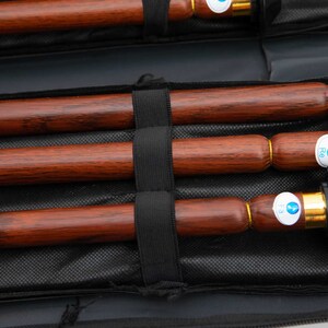 Puede incluir: Tres flautas de madera con detalles dorados y etiquetas azules se guardan en una funda de transporte negra. Las etiquetas tienen el texto "F2", "F3" y "F4".