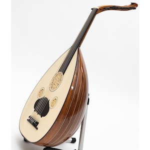 May include: A brown and white oud with intricate wood inlays and a black soundhole. The oud is on a stand and has a white background.