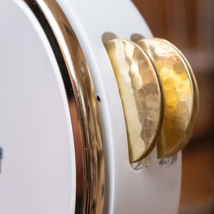 May include: A white tambourine with a gold rim and two gold cymbals. The cymbals have a hammered texture.