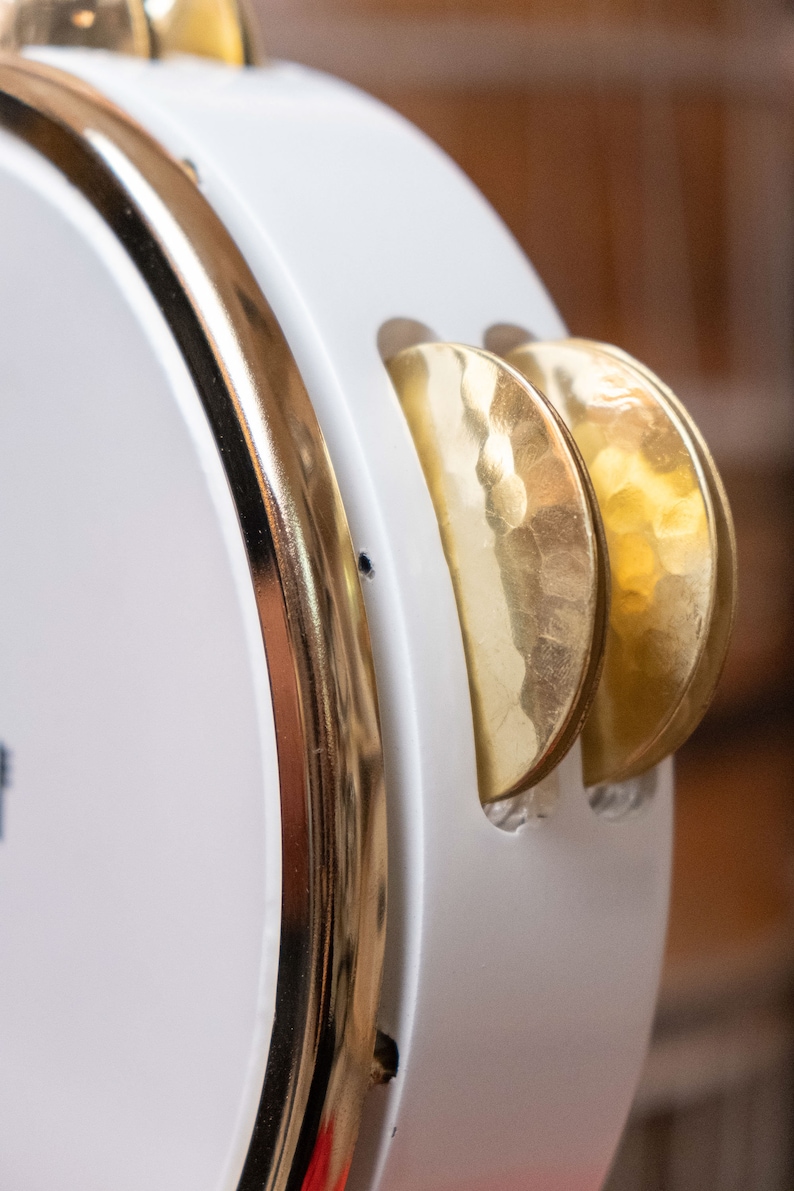 May include: A white tambourine with a gold rim and two gold cymbals. The cymbals have a hammered texture.