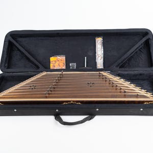 May include: A brown wooden santur, a hammered dulcimer, in a black hard-shell case with a zipper closure. The case has a handle and a black interior lining.