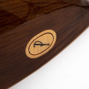 May include: Close-up of a dark brown wooden musical instrument with a light brown oval inlay featuring the letter "R".