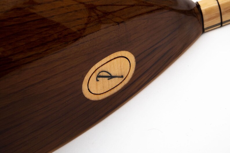 May include: Close-up of a dark brown wooden musical instrument with a light brown oval inlay featuring the letter "R".