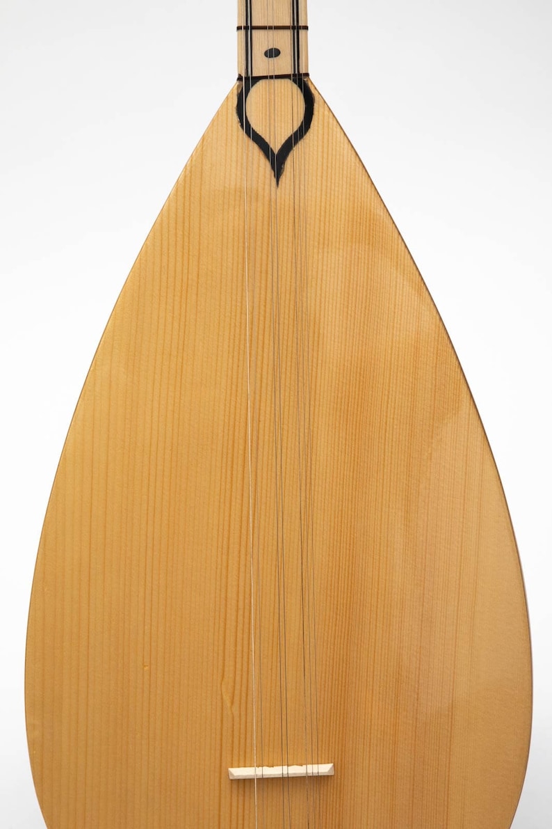 May include: A light brown wooden saz, a traditional Turkish stringed instrument, with a black heart-shaped design at the top and a white bridge at the bottom.