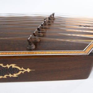 May include: A dark brown wooden santur, a hammered dulcimer, with intricate inlaid designs and silver tuning pegs.