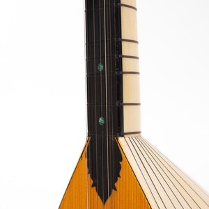 May include: A close-up of the neck and body of a wooden stringed instrument with a triangular body. The neck has black fret lines and decorative inlays. The body is made of light wood with dark wood accents.