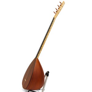 May include: A wooden long-necked stringed instrument, likely a saz or similar folk instrument, with a pear-shaped body and a long fretboard. The instrument is brown with a light-colored neck and tuning pegs. It is resting on a silver-colored stand.
