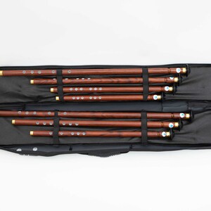 Puede incluir: Un conjunto de ocho flautas de madera en una funda de transporte negra. Las flautas est&aacute;n ordenadas por tama&ntilde;o, con la m&aacute;s grande en la parte superior y la m&aacute;s peque&ntilde;a en la parte inferior.