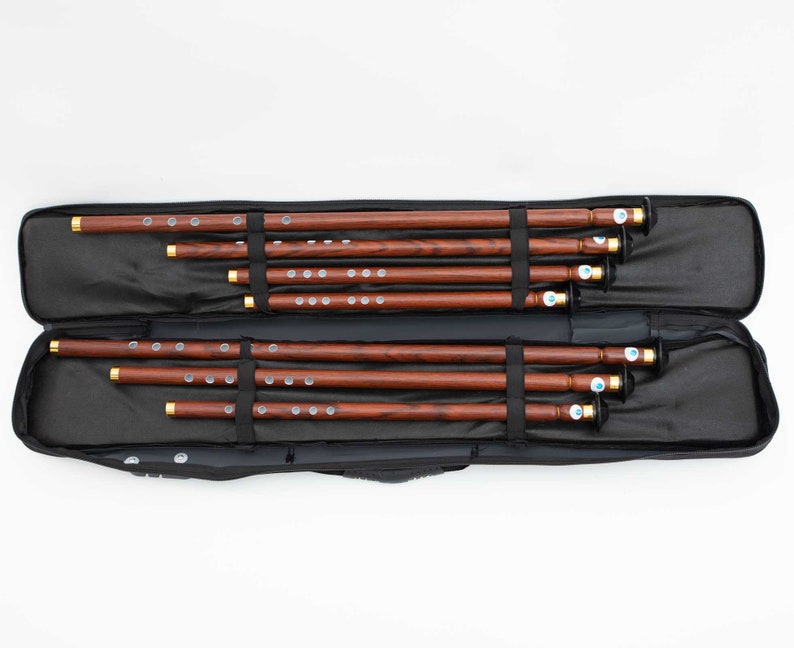 Puede incluir: Un conjunto de ocho flautas de madera en una funda de transporte negra. Las flautas est&aacute;n ordenadas por tama&ntilde;o, con la m&aacute;s grande en la parte superior y la m&aacute;s peque&ntilde;a en la parte inferior.