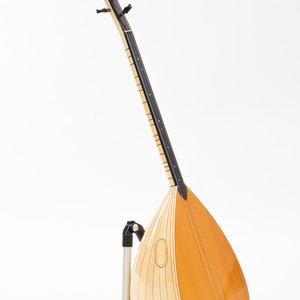 May include: A light wood and black Turkish saz, a stringed musical instrument, on a black metal stand. The saz has a pear-shaped body and a long neck with tuning pegs.
