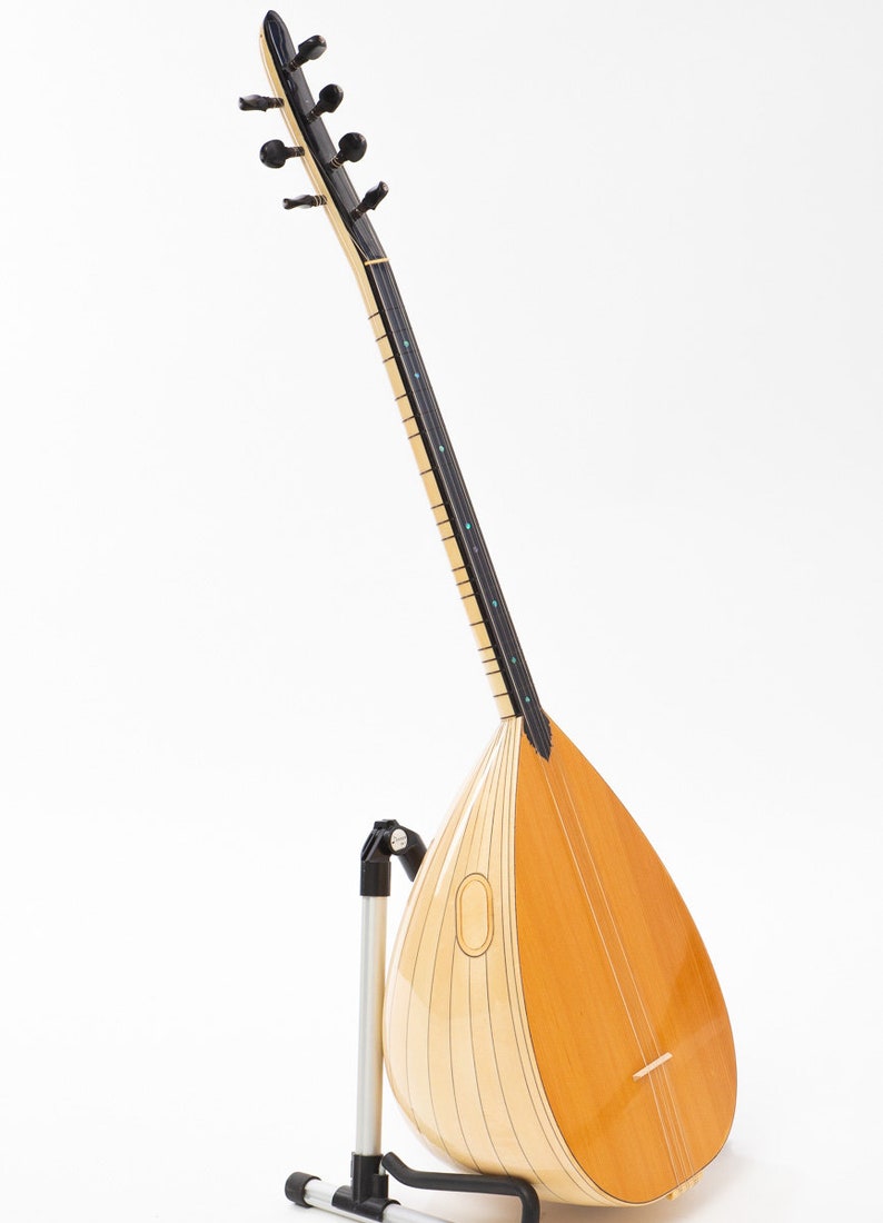 May include: A light wood and black Turkish saz, a stringed musical instrument, on a black metal stand. The saz has a pear-shaped body and a long neck with tuning pegs.
