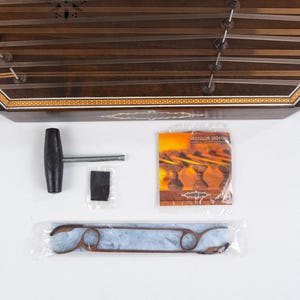 May include: A wooden santur, a hammered dulcimer, with a decorative inlay. It comes with a tuning wrench, a felt mute, a set of strings, and a pamphlet titled "Santur Music".