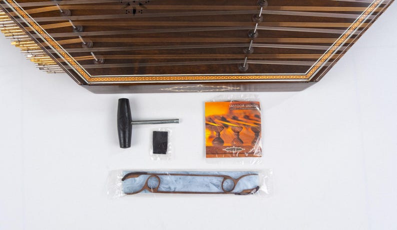 May include: A wooden santur, a hammered dulcimer, with a decorative inlay. It comes with a tuning wrench, a felt mute, a set of strings, and a pamphlet titled "Santur Music".