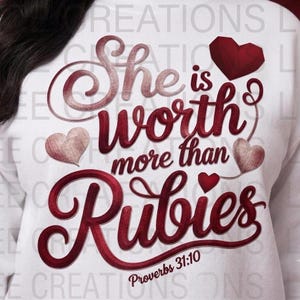 May include: A white sweatshirt featuring dark red and maroon text that reads "She is worth more than Rubies" and "Proverbs 31:10". The design includes three hearts in varying shades of red, including a geometric heart and two textured hearts.