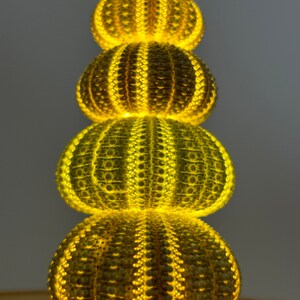 May include: A stack of four sea urchin shells illuminated from within, creating a warm yellow glow. The shells are arranged in a pyramid shape, with the largest shell at the bottom and the smallest shell at the top.