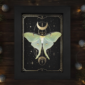 Op de afbeelding: Een ingelijste print van een groene lunavlind met gouden accenten op een zwarte achtergrond. De vlinder wordt omringd door een geometrisch ontwerp met een halve maan en sterren.