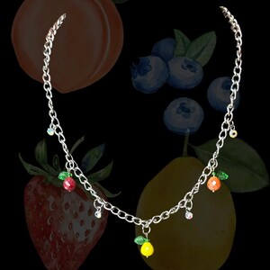 May include: A silver-toned metal chain necklace featuring multiple dangling charms, including small faceted fruit shapes in red, yellow, and orange with green leaves, interspersed with tiny clear iridescent crystal beads along the link chain.