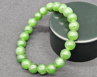 May include: A green jade bead bracelet with round beads. The bracelet is on a black surface.