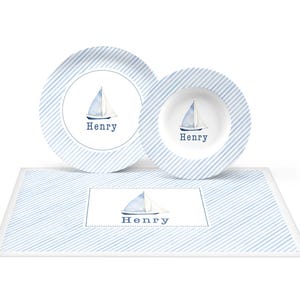 May include: A blue and white striped placemat with a white plate and bowl featuring a sailboat and the name "Henry".