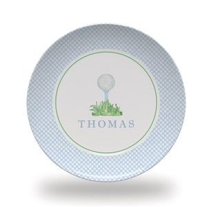 May include: A white ceramic plate with a blue and white gingham pattern. The center of the plate features a green circle with a white golf ball on a tee and green grass. The name "THOMAS" is written in black below the golf ball.