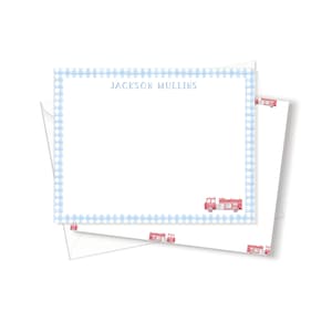 May include: Blue and white gingham stationery with the name "Jackson Mullins" printed at the top. The stationery is folded in half and has a red fire truck illustration on the bottom right corner.