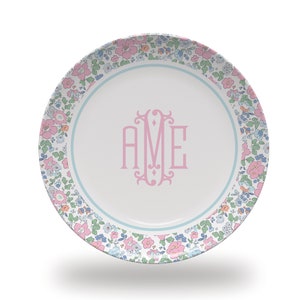 May include: A white ceramic plate with a blue and pink floral border. The center of the plate features a pink monogram "AME".