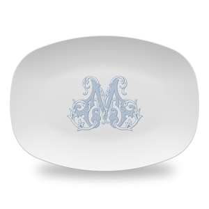 May include: A white oval serving platter with a blue decorative monogram of the letter "M" in a stylized font.