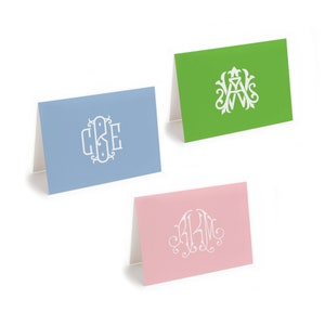 May include: Three blank folded cards with white monogrammed initials on each. The cards are light blue, green, and pink.