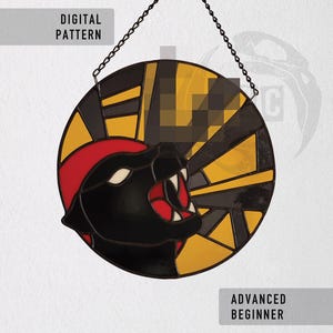 Pode incluir: Um design circular em vitral com uma pantera negra com detalhes vermelhos, sobre um fundo amarelo e preto. Inclui os textos "DIGITAL PATTERN" e "ADVANCED BEGINNER". Suspenso por uma corrente.
