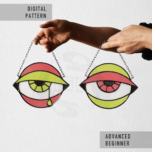 Peut inclure: Deux ornements en vitrail en forme d'œil avec des chaînes de suspension. Chaque œil présente un iris blanc, une paupière supérieure rouge et jaune, et un contour noir. Un œil a une larme. Le texte "DIGITAL PATTERN" et "ADVANCED BEGINNER" est également visible.
