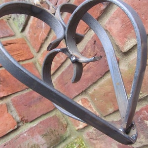 May include: A metal heart-shaped sculpture with a decorative design. The sculpture is made of two intertwined hearts, creating a unique and intricate pattern. The metal has a dark, aged finish, giving it a rustic look.