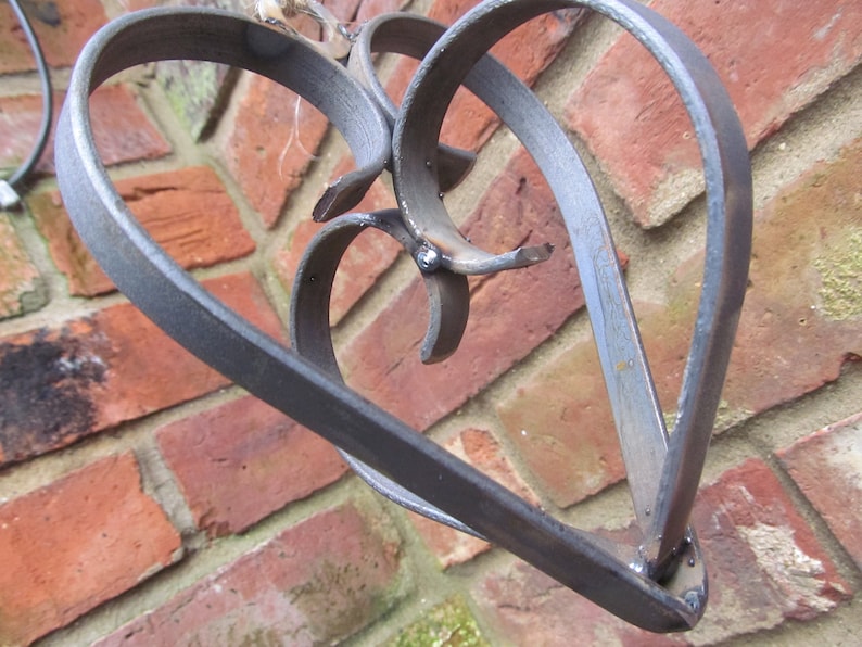 May include: A metal heart-shaped sculpture with a decorative design. The sculpture is made of two intertwined hearts, creating a unique and intricate pattern. The metal has a dark, aged finish, giving it a rustic look.