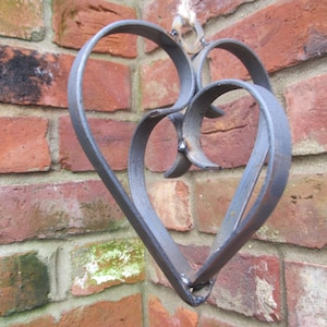 May include: A metal heart-shaped wall decor with a double heart design. The heart is made of dark gray metal and has a rustic finish.