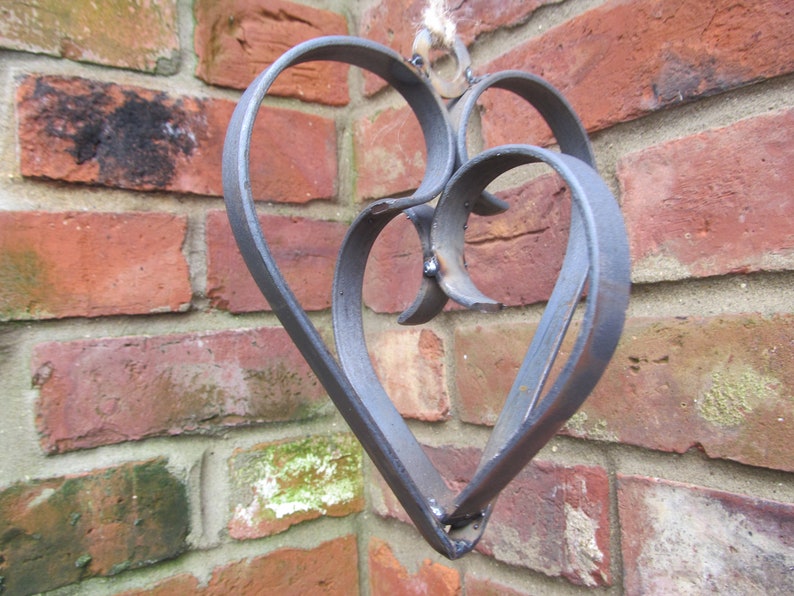 May include: A metal heart-shaped wall decor with a double heart design. The heart is made of dark gray metal and has a rustic finish.