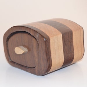 May include: A small wooden box with a sliding drawer. The box is made of dark wood with light wood stripes. The drawer has a small wooden knob.