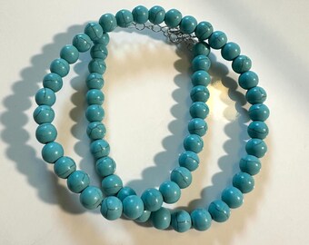 May include: A turquoise beaded necklace with a silver clasp. The necklace is made of round beads and is approximately 18 inches long.