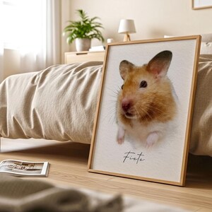 May include: A rectangular framed print featuring a portrait of a golden-brown and white hamster with dark eyes and whiskers. The name Fiete is printed in black cursive script below the hamster. The print is housed in a light wood frame.