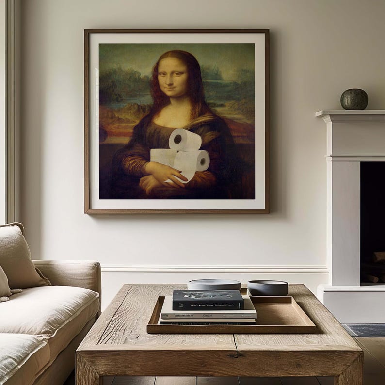 K&ouml;nnte beinhalten: Gerahmter Druck der Mona Lisa, die Toilettenpapierrollen h&auml;lt. Das Kunstwerk befindet sich in einem dunklen Holzrahmen und h&auml;ngt &uuml;ber einem Holztisch. Der Raum hat neutral get&ouml;nte W&auml;nde und einen Kamin.