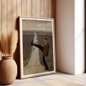 May include: A framed rectangular wall art print featuring a surreal composition of a man in a brown blazer and dark trousers standing on a road, with one leg raised high, superimposed over a muted landscape painting with a long, straight road.