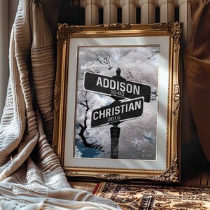 Puede incluir: Una impresión enmarcada de una señal de calle con los nombres "Addison" y "Christian" en ella. La señal está colocada sobre un fondo de escena de bosque nevado. La fecha "10-02" está en la señal de Addison y la fecha "2015" está en la señal de Christian.
