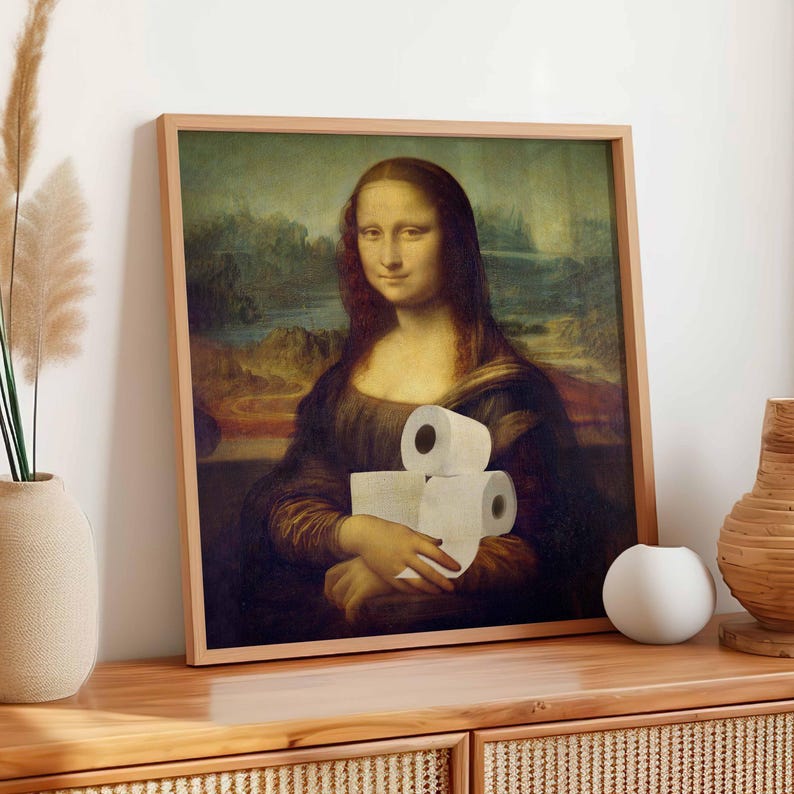K&ouml;nnte beinhalten: Gerahmter Druck der Mona Lisa, die drei Rollen Toilettenpapier h&auml;lt. Das Kunstwerk befindet sich in einem Holzrahmen und wird auf einem Holzschrank ausgestellt. Der Hintergrund des Kunstwerks zeigt eine Landschaft mit Bergen und einem Fluss.