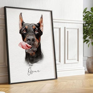 May include: A framed wall art print featuring a watercolor-style portrait of a black and tan Doberman Pinscher dog with its tongue out, positioned above the name Oscar written in a black cursive script on a textured white background.
