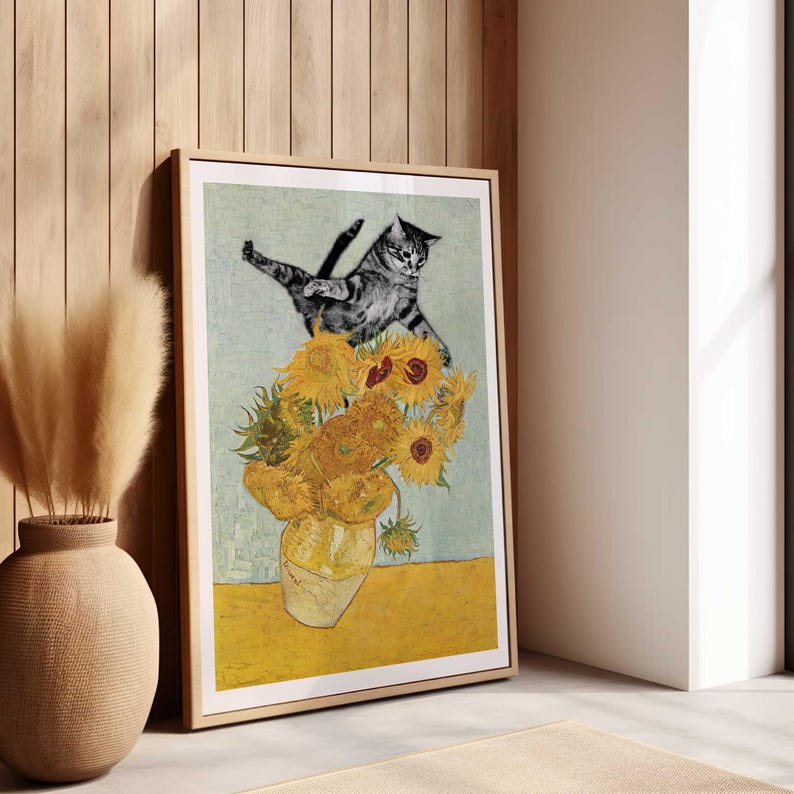 Puede incluir: Una impresi&oacute;n enmarcada de un gato saltando sobre un jarr&oacute;n de girasoles. El gato es gris y blanco, y los girasoles son amarillos con centros marrones. El fondo es azul claro.