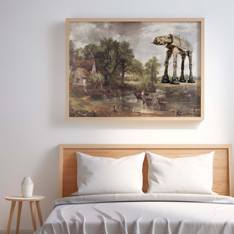 May include: A framed print featuring a landscape painting with a river, trees, and a building. An AT-AT walker from Star Wars is digitally added to the top right corner. The frame is a light brown color.